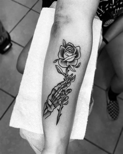 A Person With Tattoos On Their Hands Holding Up A Skull And Flower